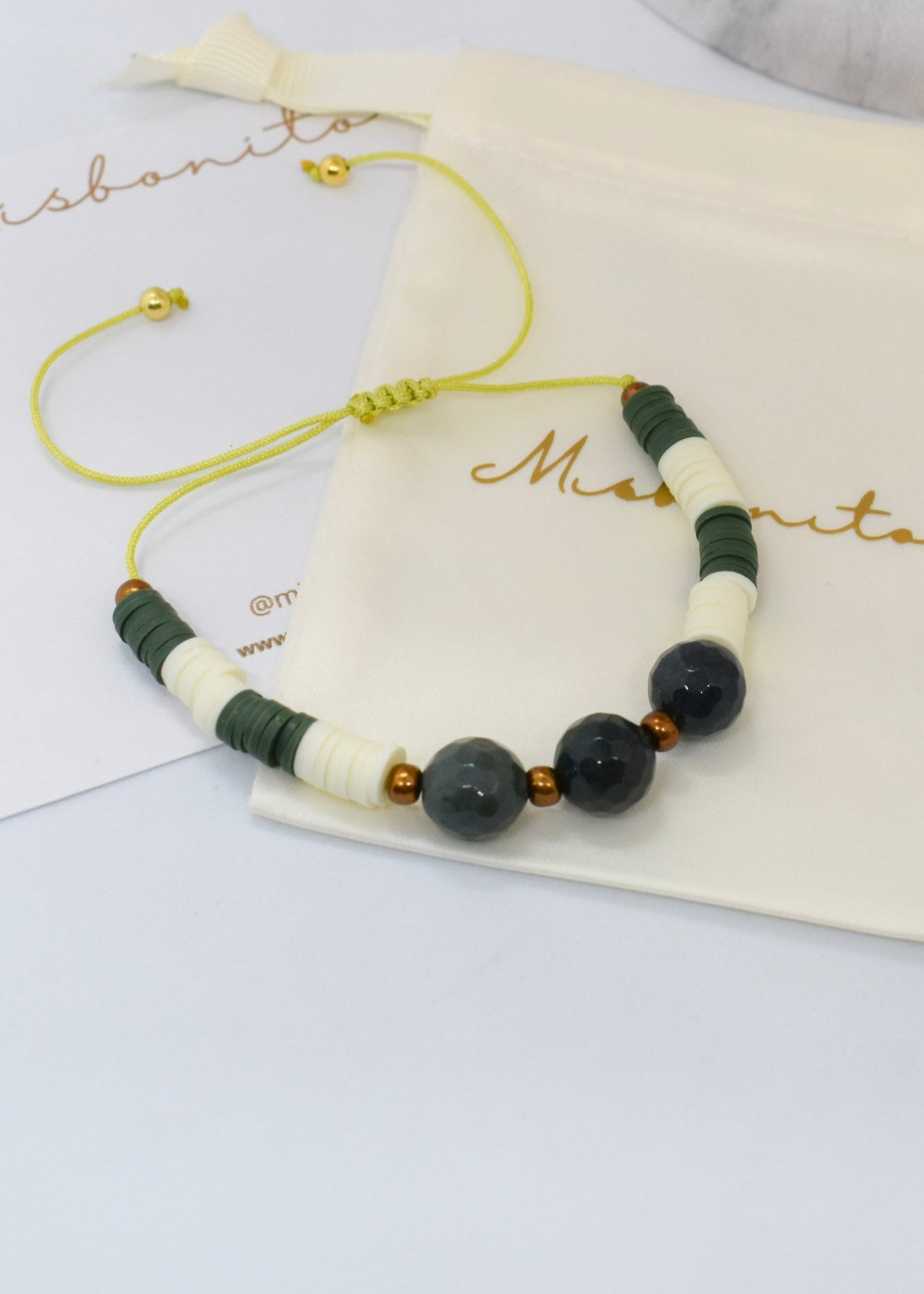 Beaded bracelet with green and white beads on a branded pouch