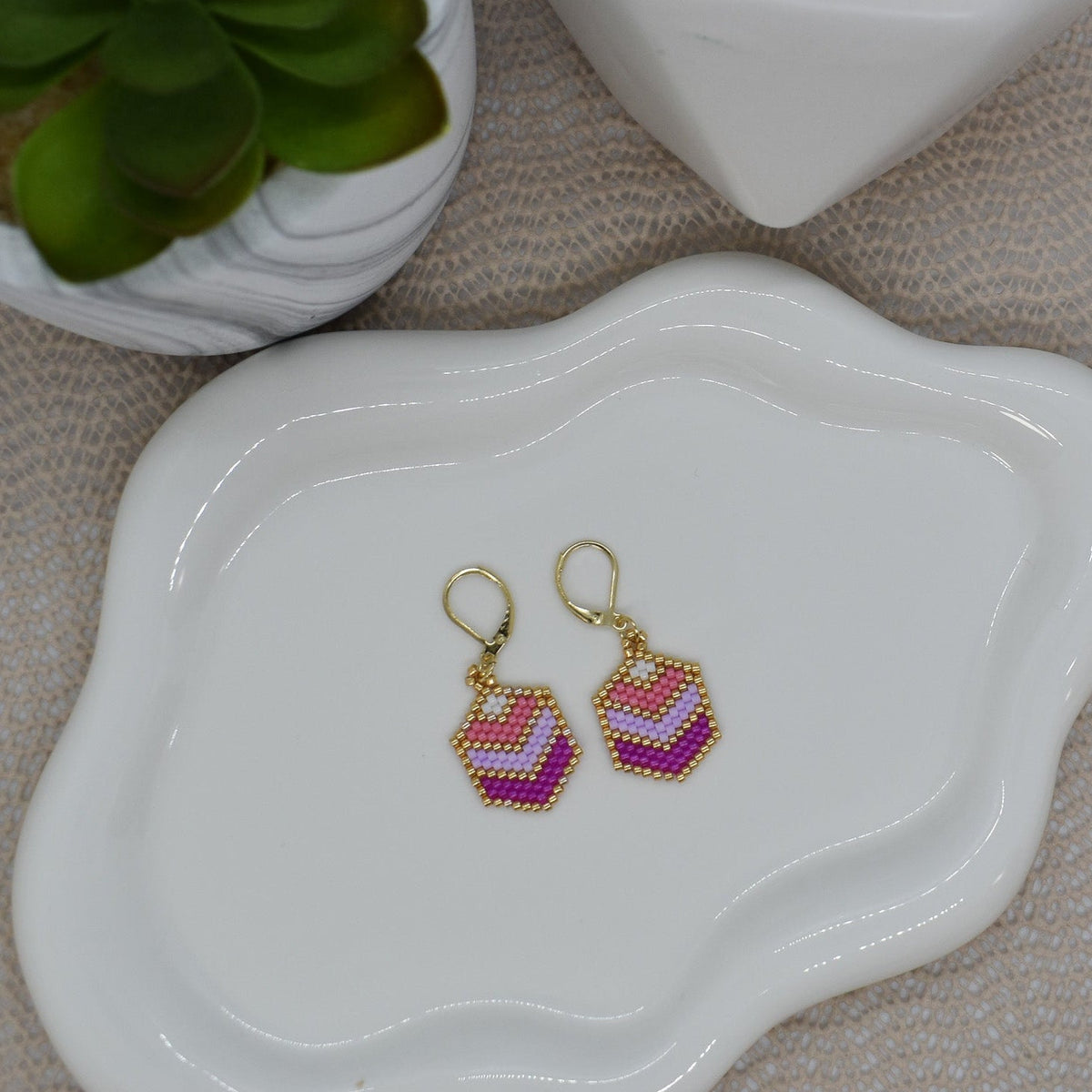 Beaded earrings on a white dish with a plant and decorative item in the background