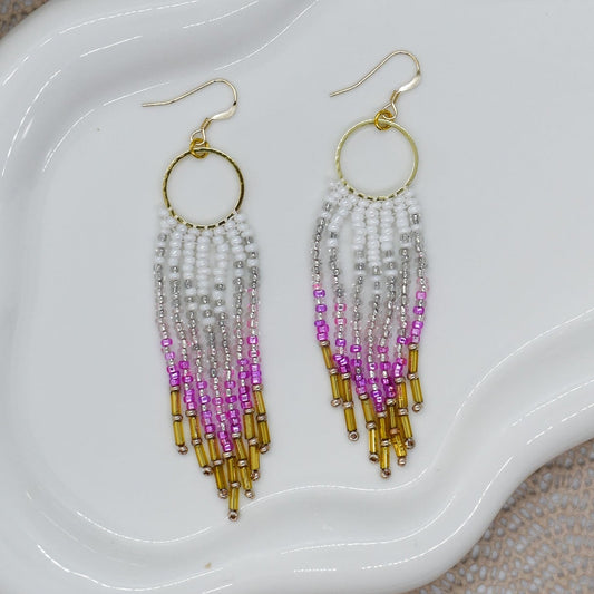 Beaded earrings with gold, pink, and purple on a white dish.