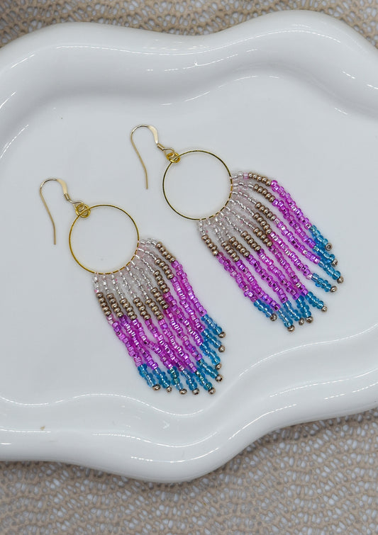 Beaded earrings with pink and blue gradient on a white dish