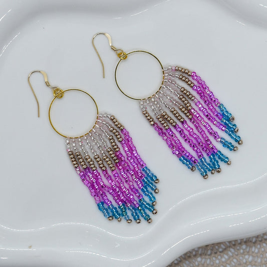 Beaded earrings with pink and blue gradient on a white dish