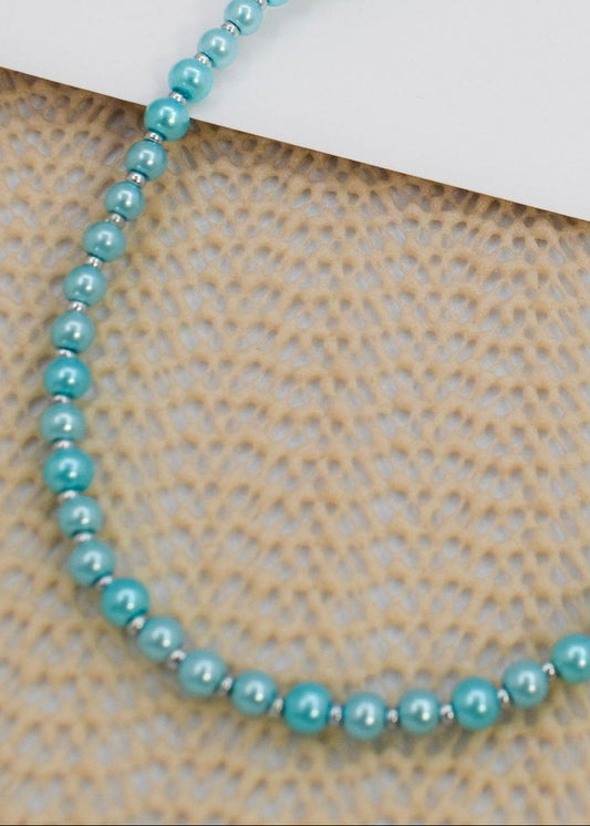 Blue beaded necklace on a textured surface with a white card