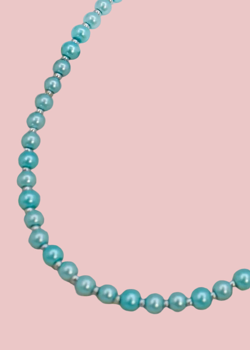 Blue beaded necklace on a textured surface with a white card