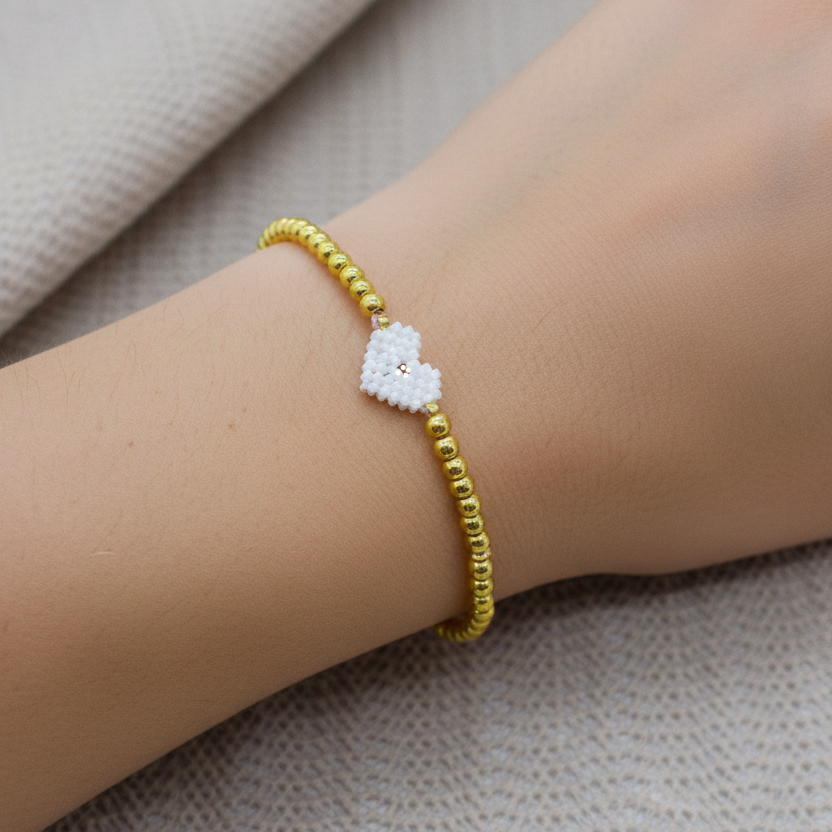 Gold bracelet with a heart-shaped charm on a wrist against a neutral background