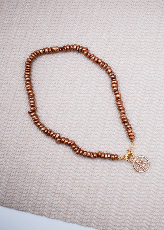 Brown beaded necklace with a pentacle charm on a textured surface