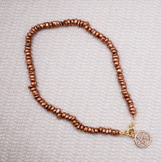 Brown beaded necklace with a pentacle charm on a textured surface