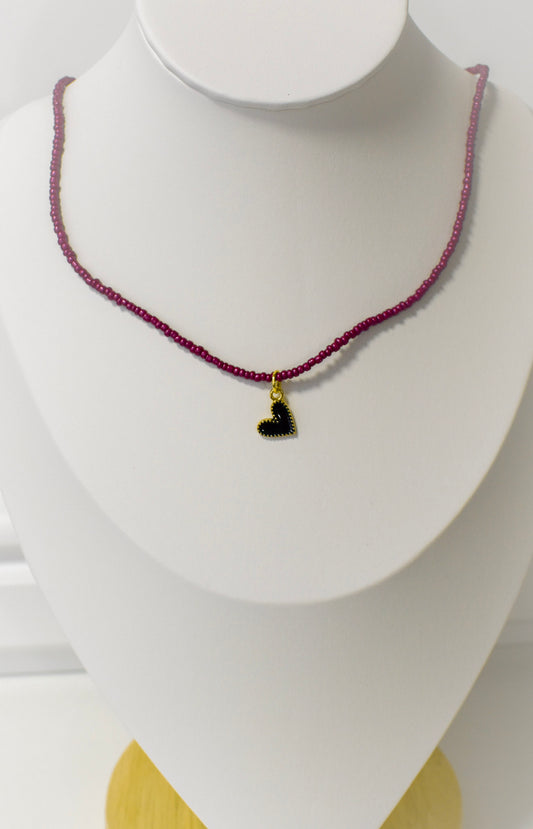 Burgundy beaded necklace with a black heart pendant on a mannequin