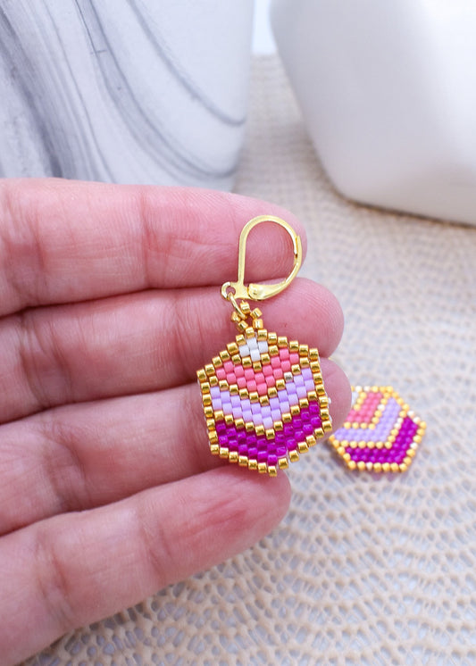 Colorful beaded earrings held in a hand with a marble background