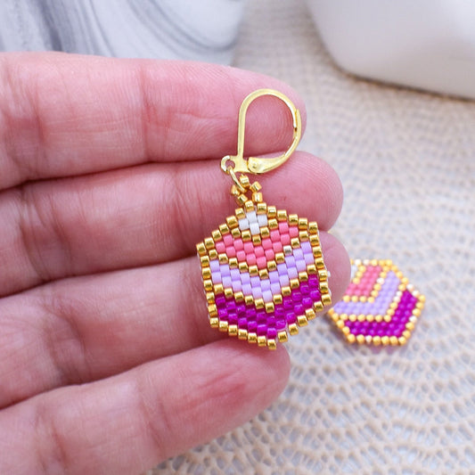 Colorful beaded earrings held in a hand with a marble background