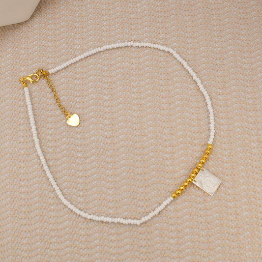 Necklace with white beads and gold chain on a beige surface