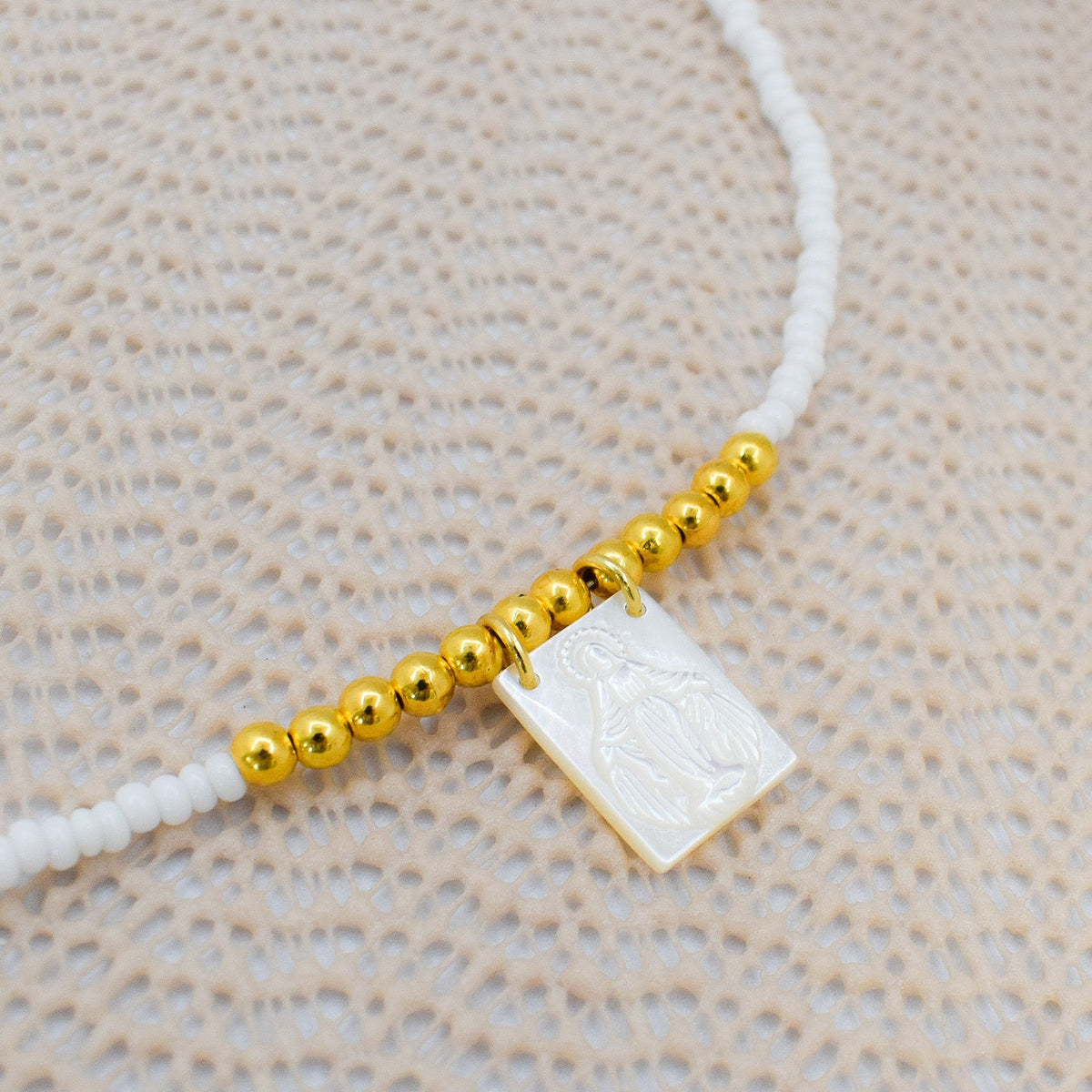 Necklace with gold beads and a square white stone on a beige textured background
