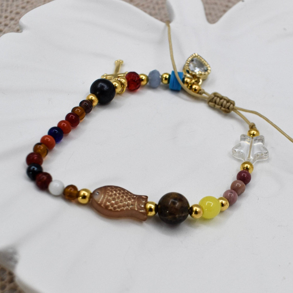 A beaded bracelet with a carved brown fish charm, gold spacer beads, and assorted colored beads, displayed on a white ceramic dish.