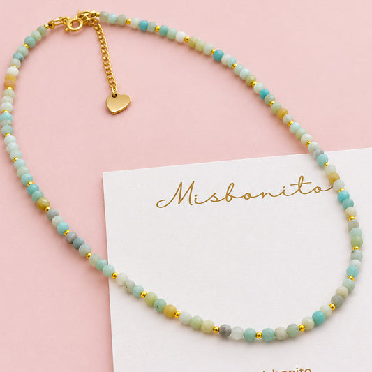 Mini Amazonite beads bracelet with light blue-green beads and gold-tone details, displayed on a white misbonito card on a beige textured fabric background.