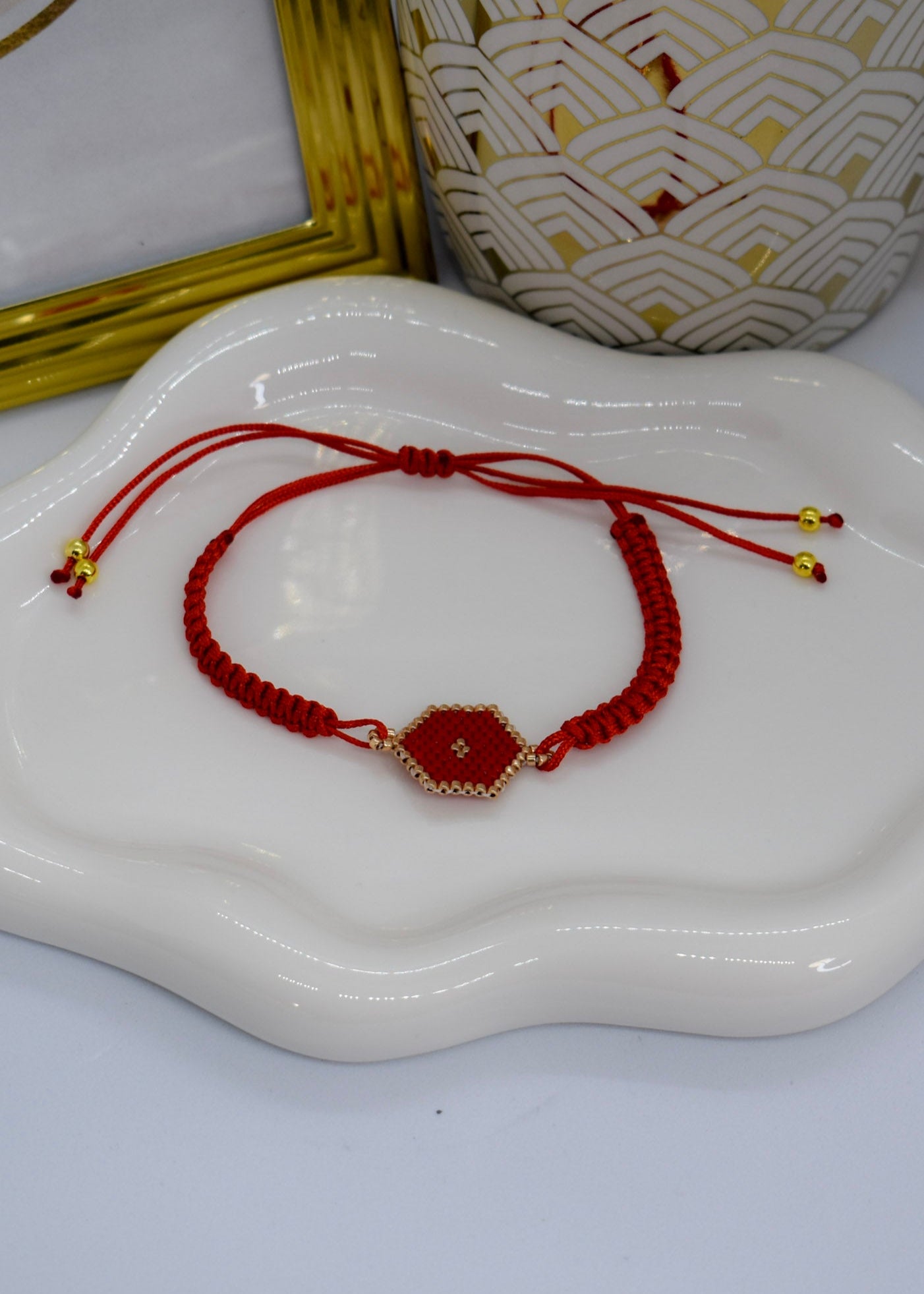 Red string bracelet with a gold charm on a white dish