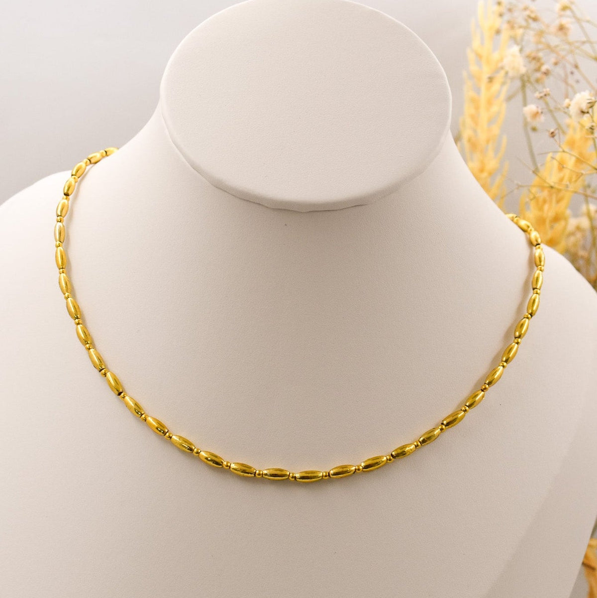 Gold necklace on a white mannequin bust with a neutral background