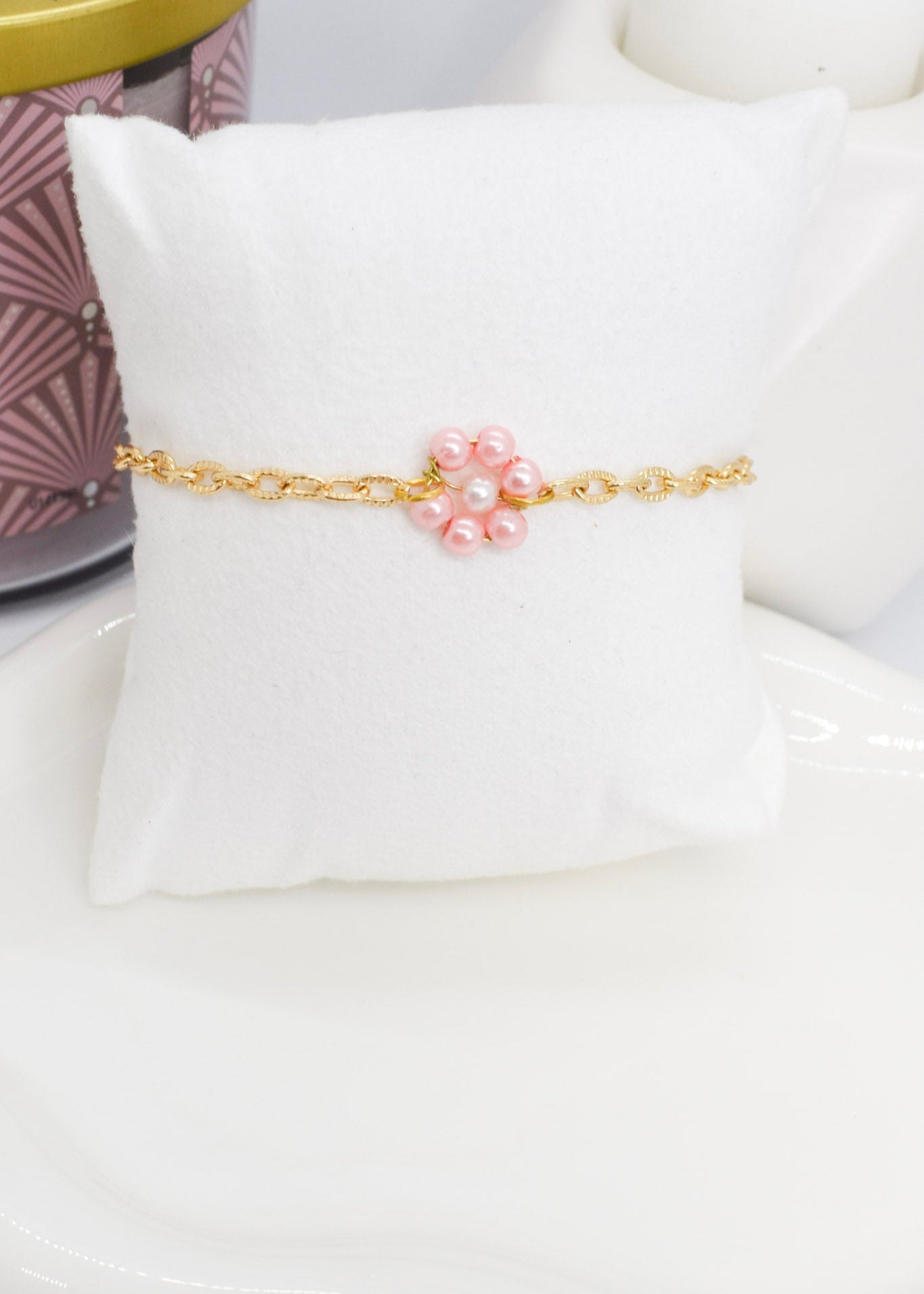 Gold bracelet with pink daisy flower made with pearls on a white cushion