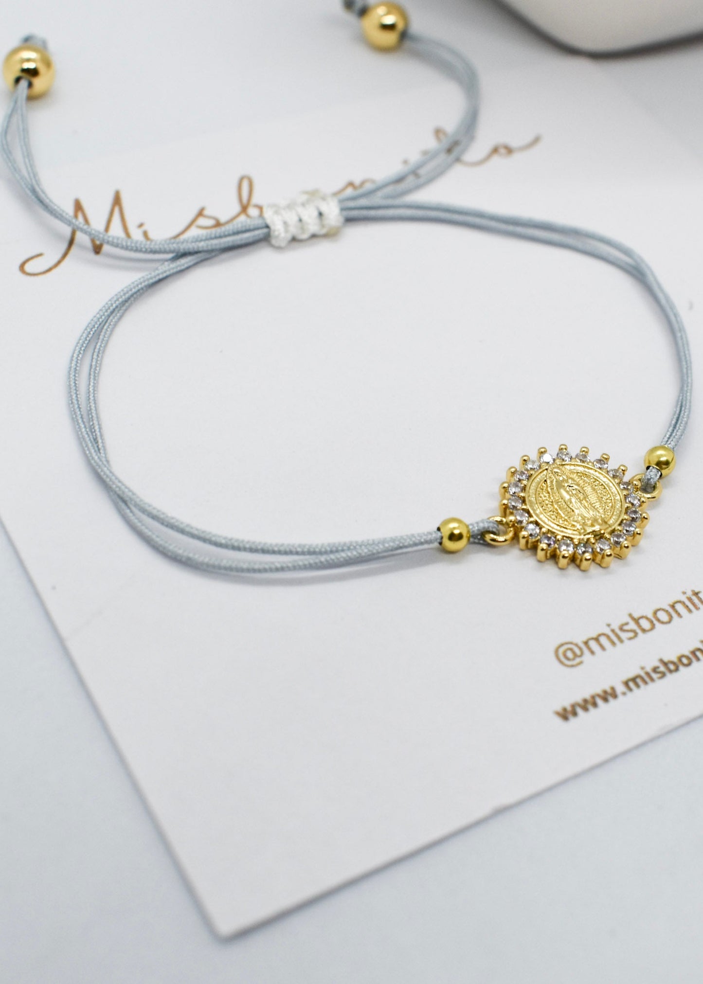 Gray bracelet with gold charm on a white card with 'misbonito' branding