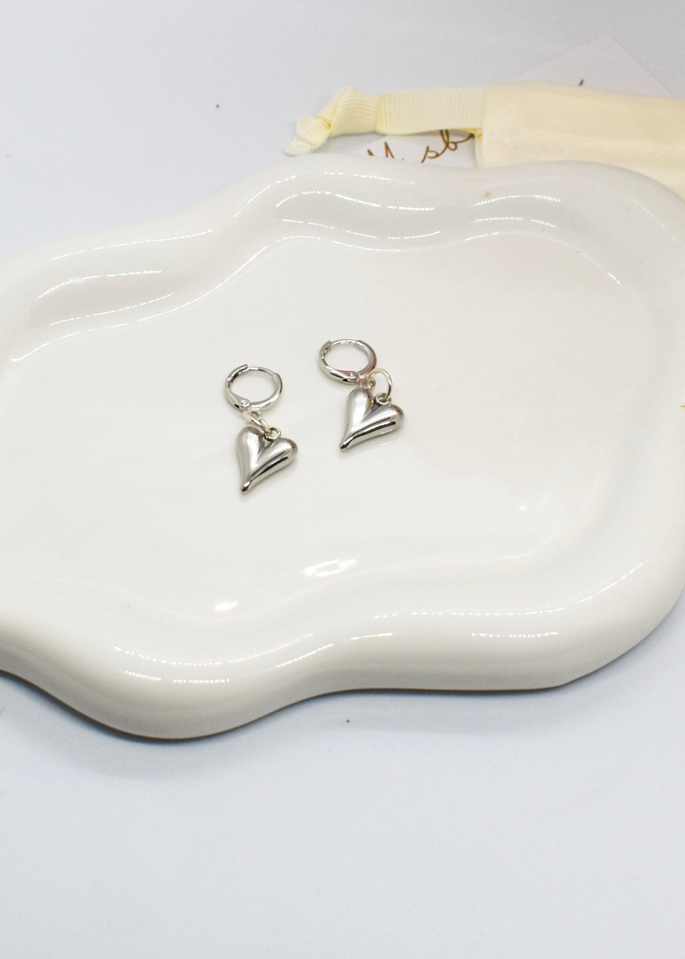 Heart-shaped silver earrings on a white dish with a white background