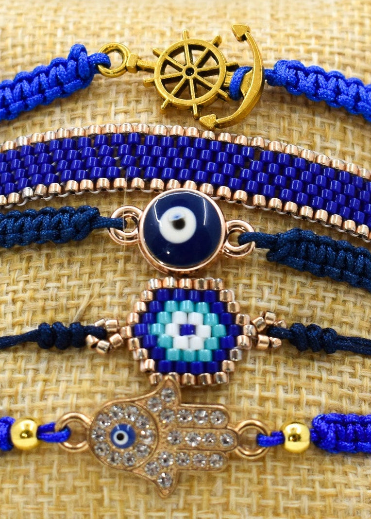 Set of blue and gold bracelets with evil eye and hamsa hand designs on a textured surface.