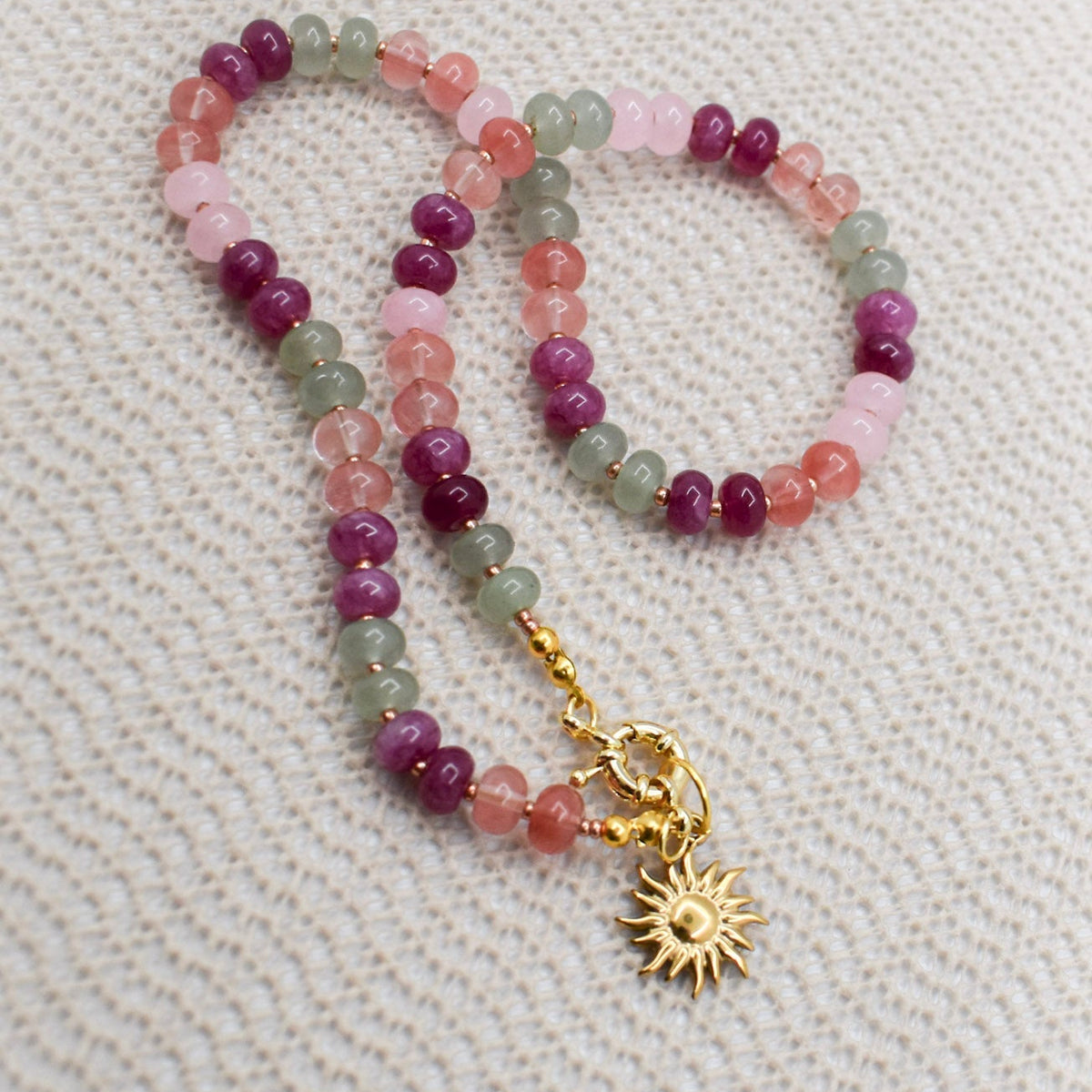 Multicolored beaded necklace with a gold charm on a textured beige background