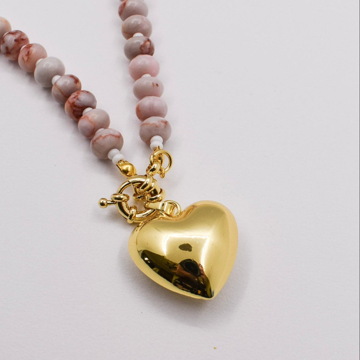 Necklace with pink beaded chain and gold heart pendant on a white background