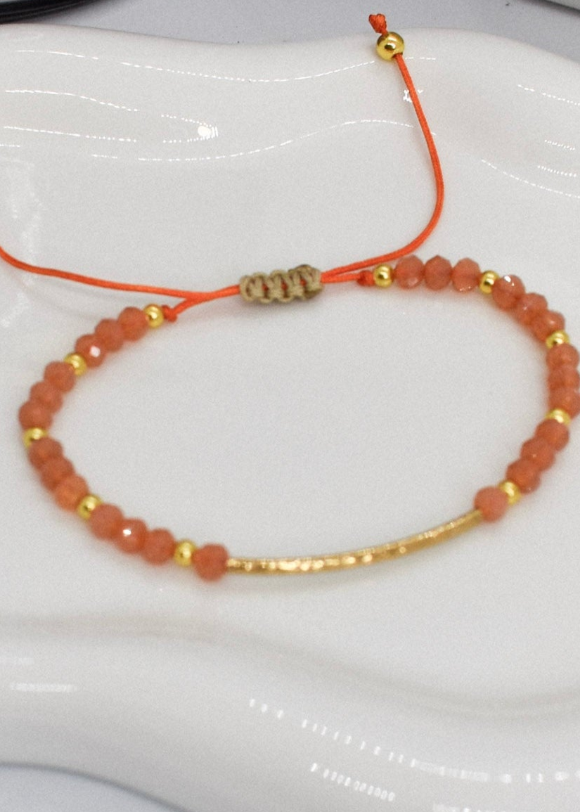 Beaded bracelet with orange beads and gold accents on a white surface