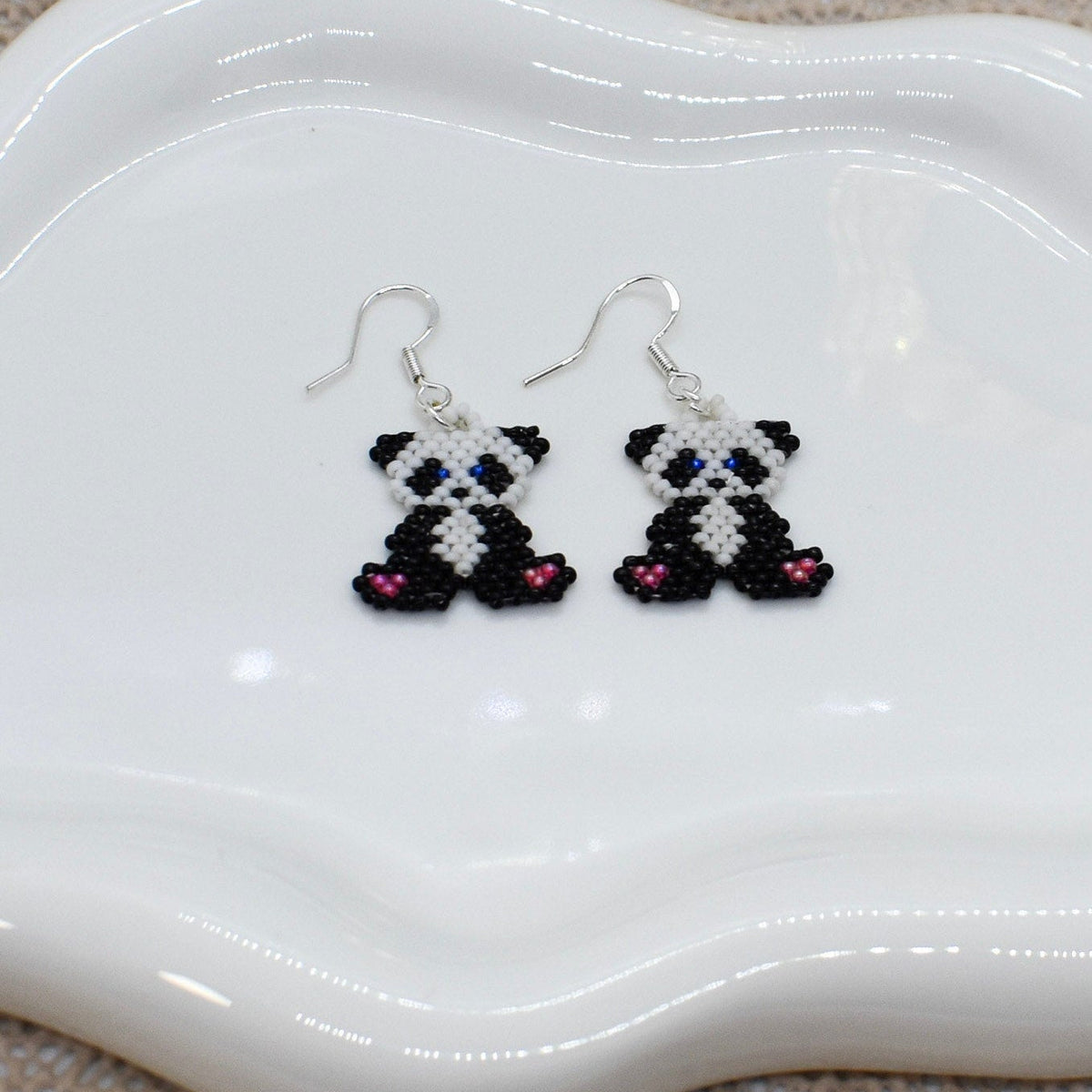 Panda-shaped earrings on a white dish with a textured surface