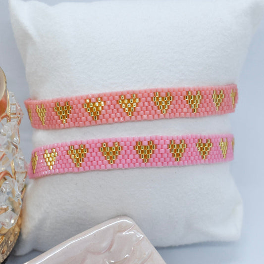 Pink bracelet with gold heart patterns on a white cushion