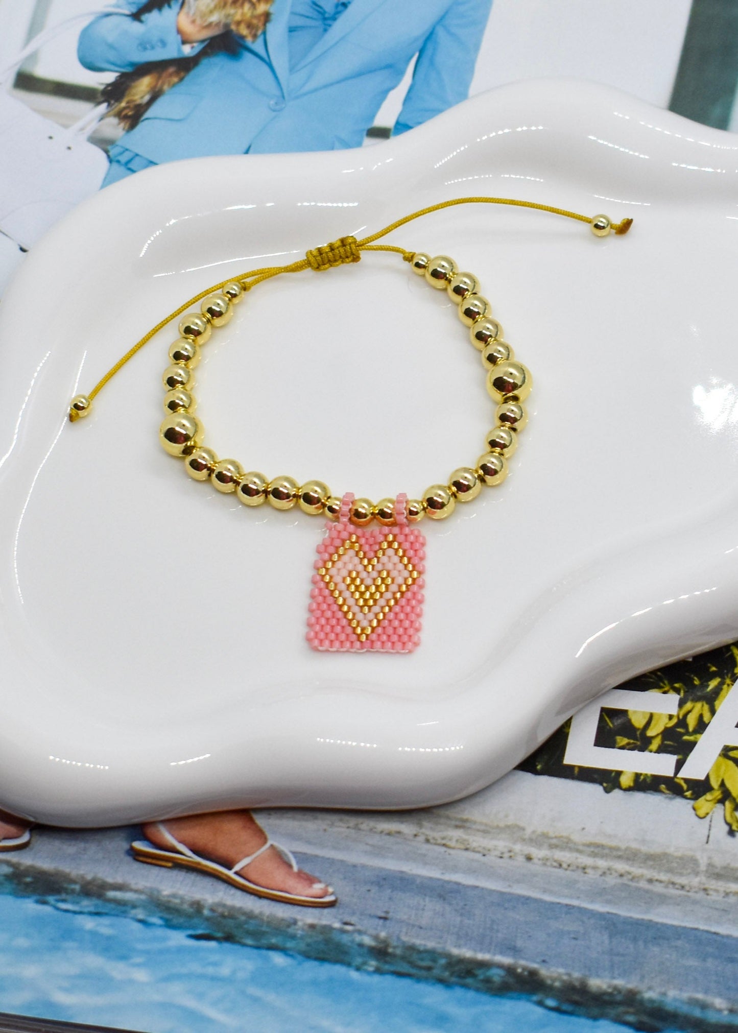 Bracelet with a pink heart charm on a white ceramic dish.