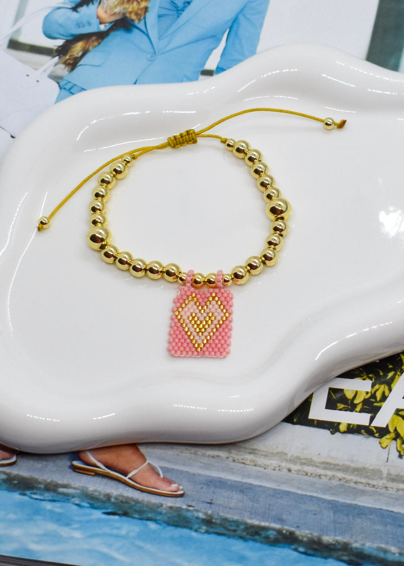Bracelet with a pink heart charm on a white ceramic dish.