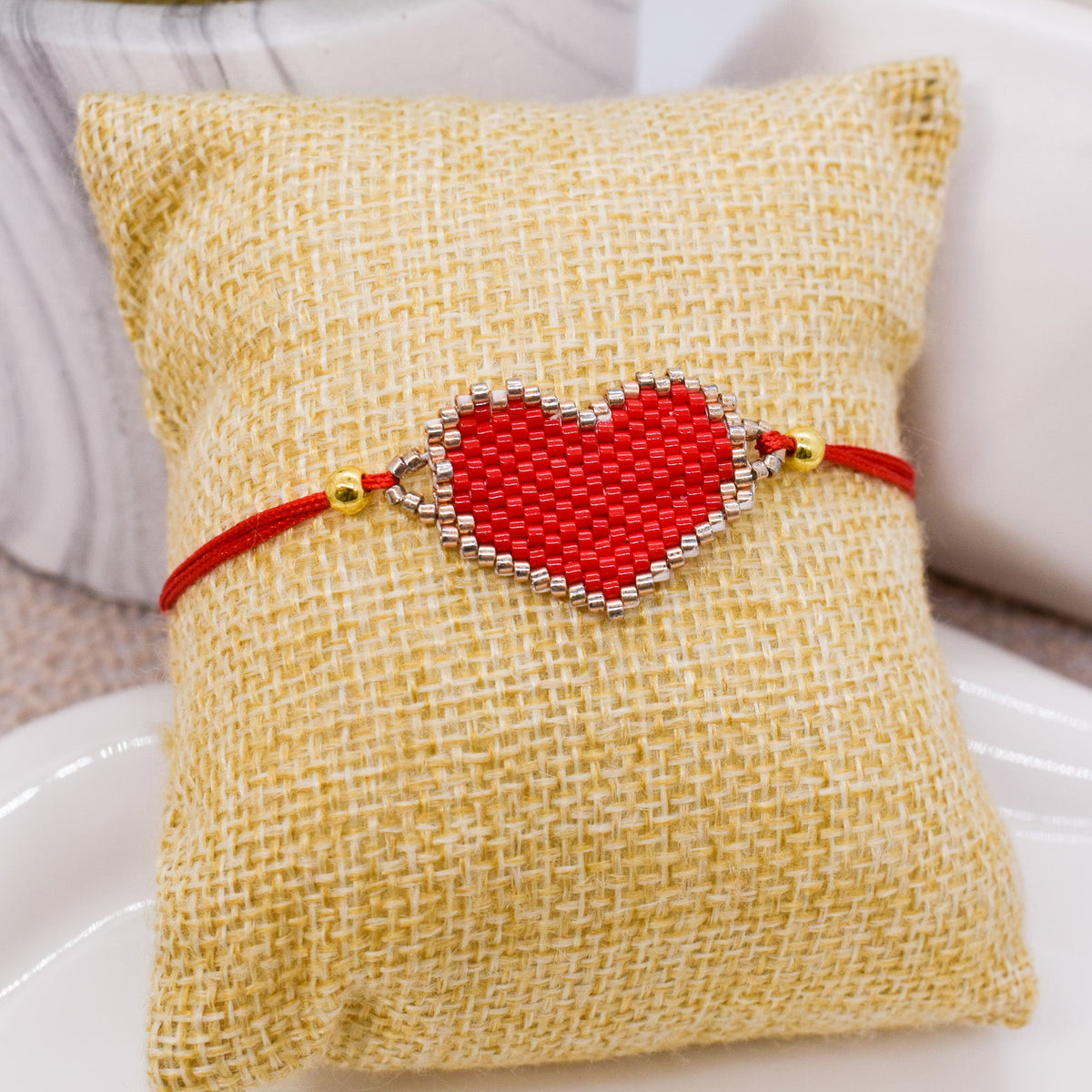 Red heart-shaped beaded bracelet on a textured beige pillow with a blurred background