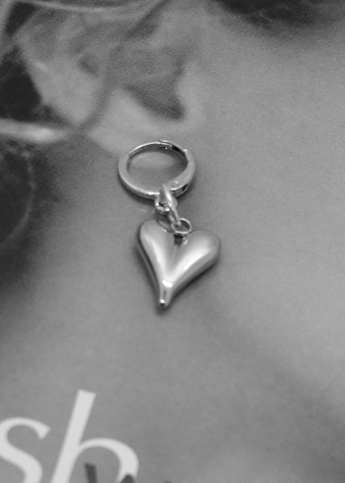 Silver heart-shaped earring worn by a person with a blurred background