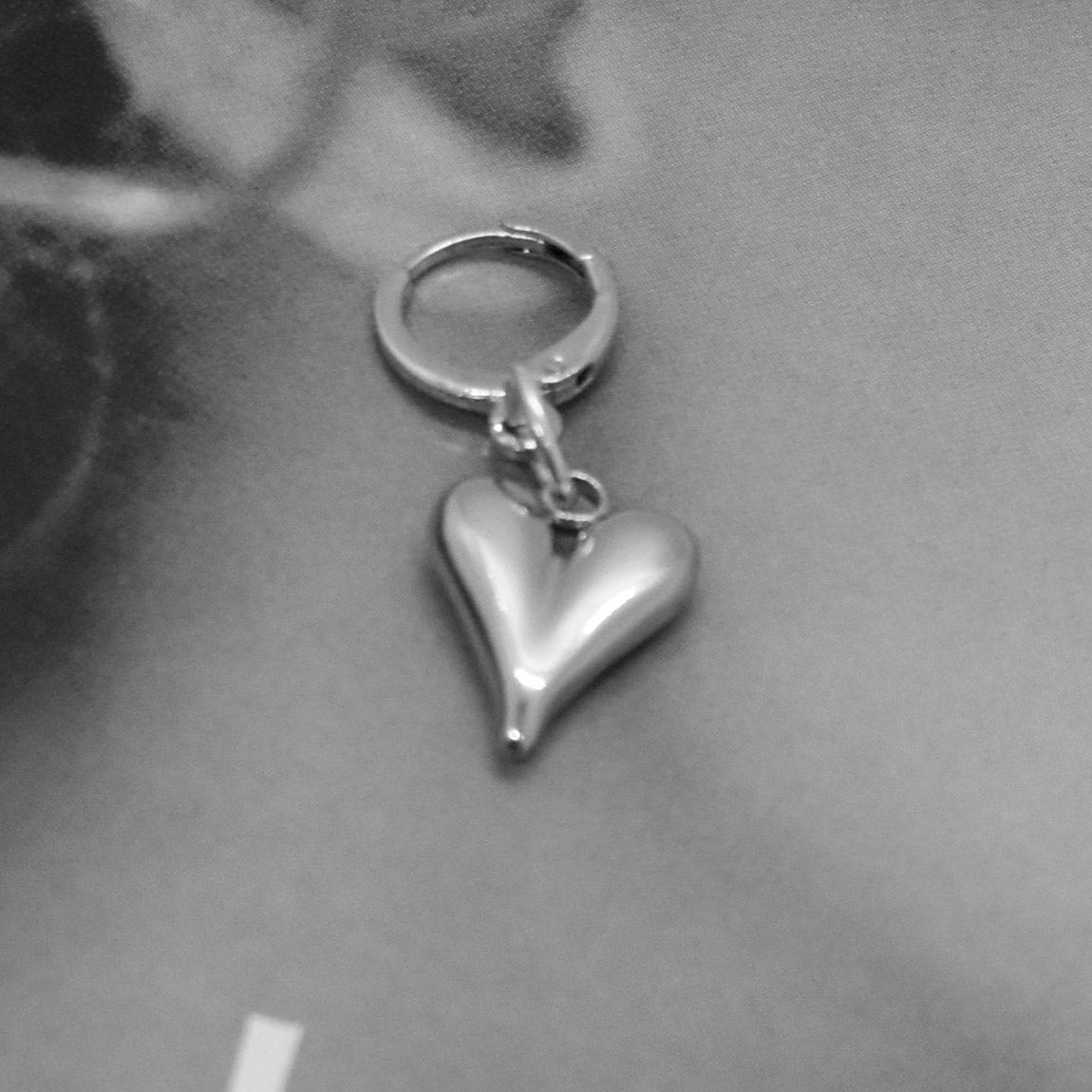 Silver heart-shaped earring worn by a person with a blurred background