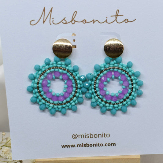 Turquoise and purple beaded earrings on a Misbonito branded card with a wooden stand.