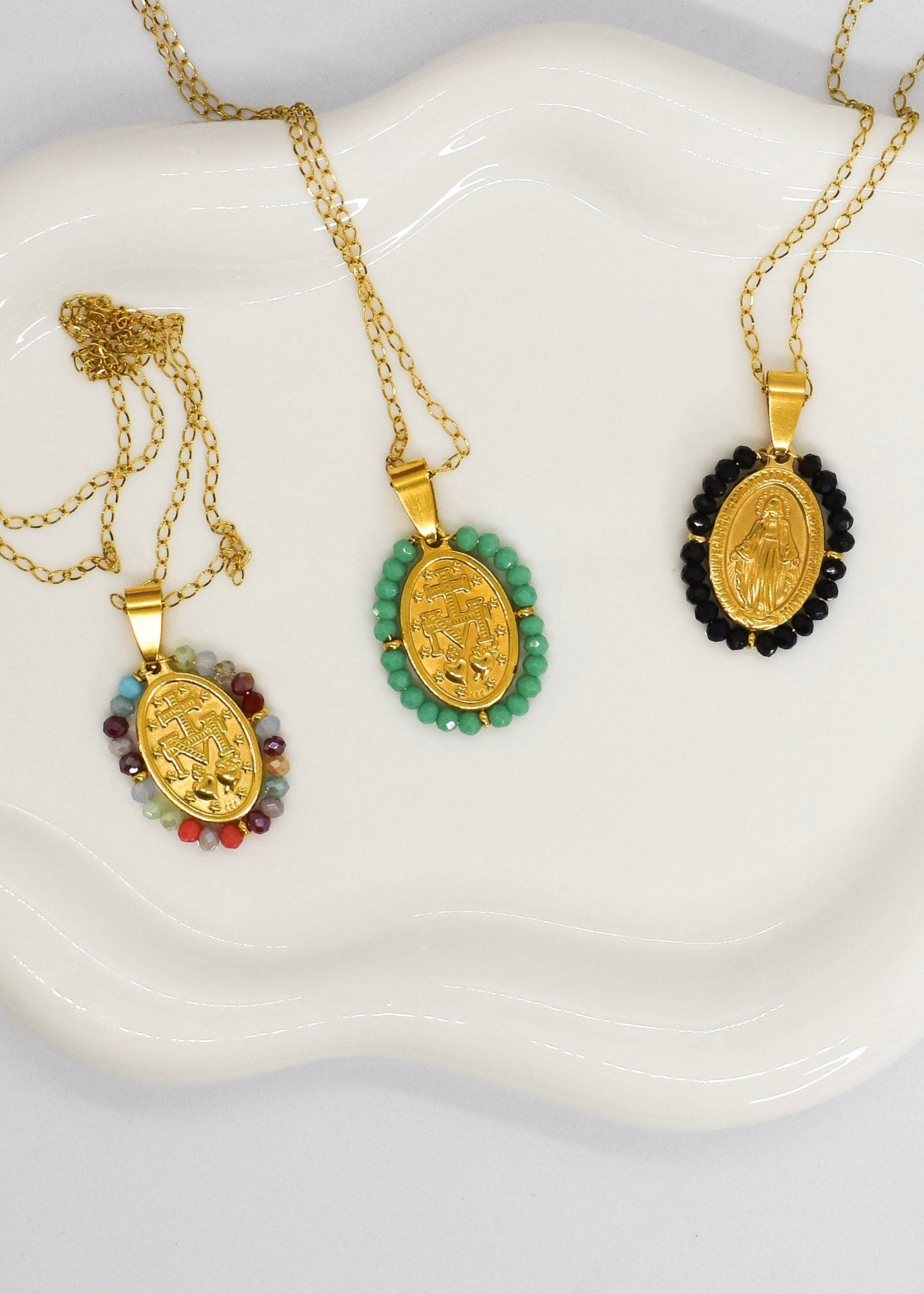 Three gold necklaces with pendants on a white dish
