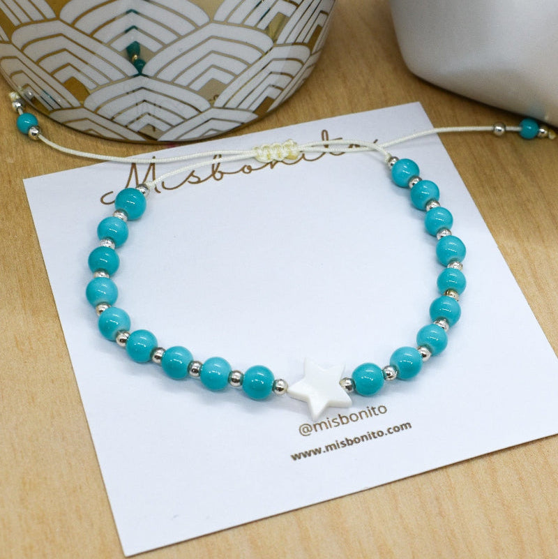 Turquoise beaded bracelet on a white card with 'Mishbonito' branding on a wooden surface.