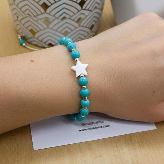 Turquoise beaded bracelet with a star charm on a wrist, with a blurred background.