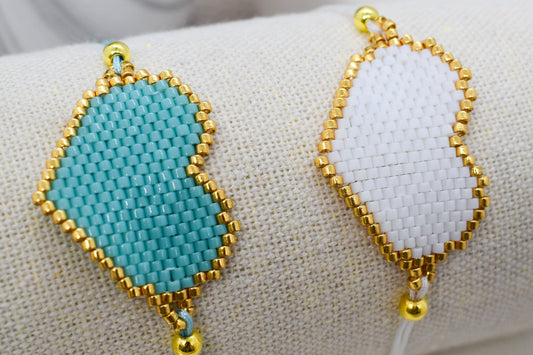 Two beaded bracelets, one turquoise and one gold, on a white fabric background.