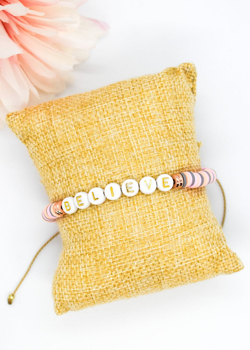 Bracelet with 'BELIEVE' beads on a yellow textured pillow with flowers in the background