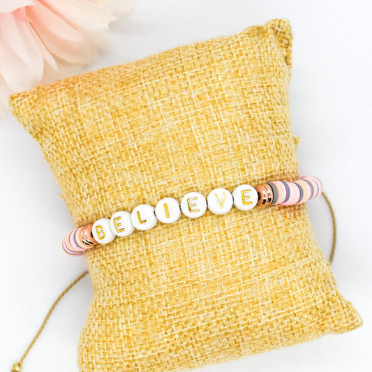 Bracelet with 'BELIEVE' beads on a yellow textured pillow with flowers in the background