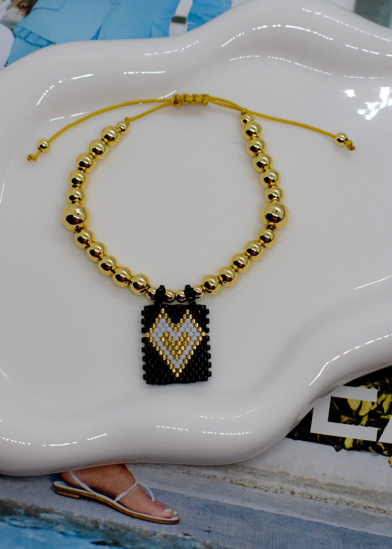 Gold beaded necklace with a black and gold pendant on a white decorative object.