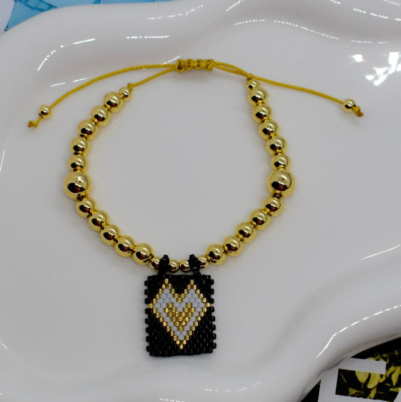 Gold beaded necklace with a black and gold pendant on a white decorative object.