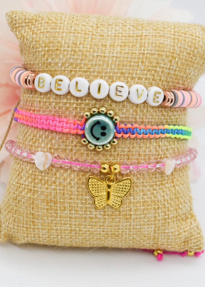 Set of colorful bracelets with butterfly charms on a textured pillow