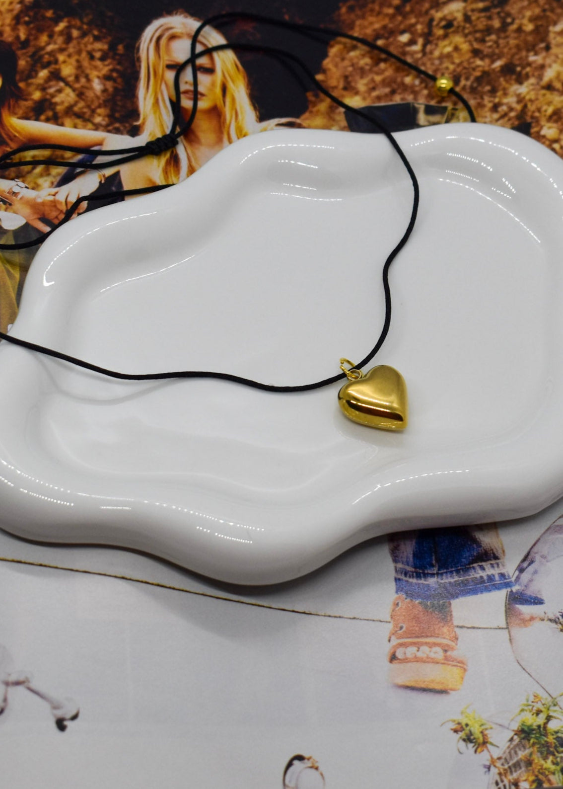 Gold heart-shaped pendant on a black cord with a white dish on top of a magazine