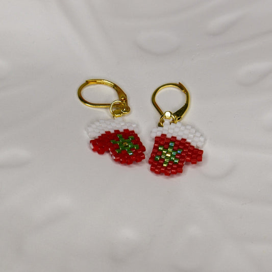 Gold earrings with red Christmas mitten designs on a white ceramic tray