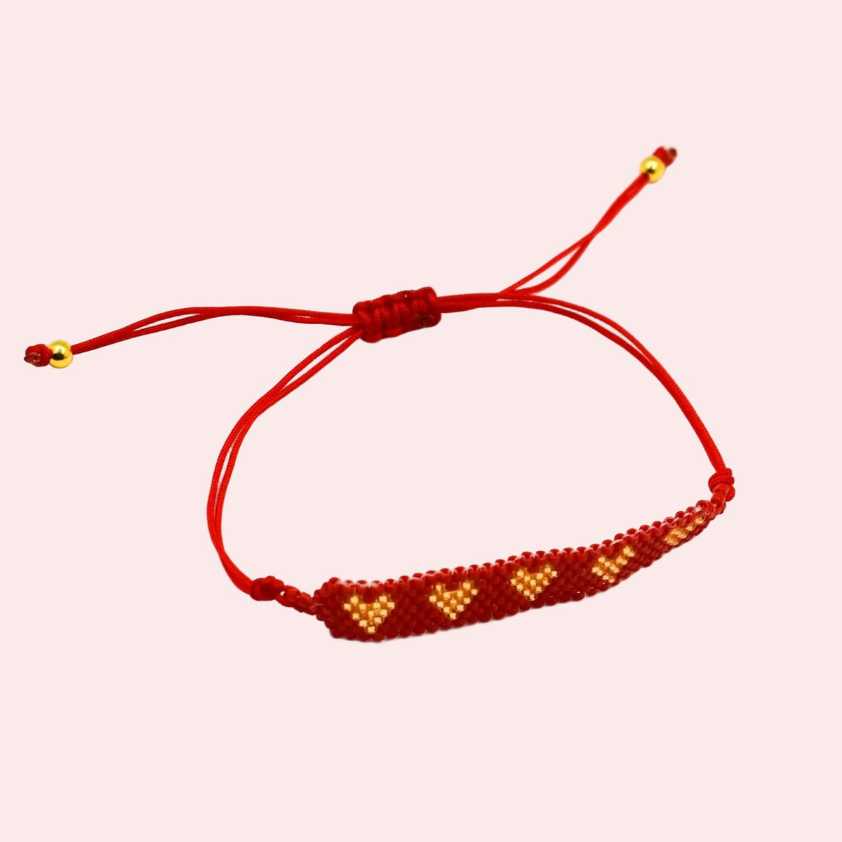 A red cord bracelet with a beaded bar featuring golden and red geometric patterns, shown on a plain white background.