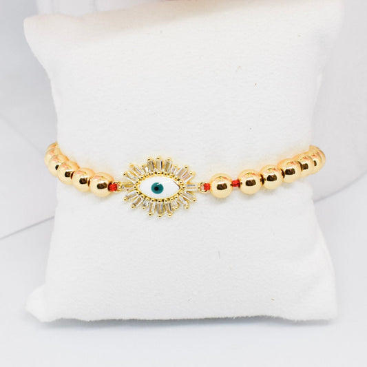 Gold bracelet with a central eye design on a white cushion