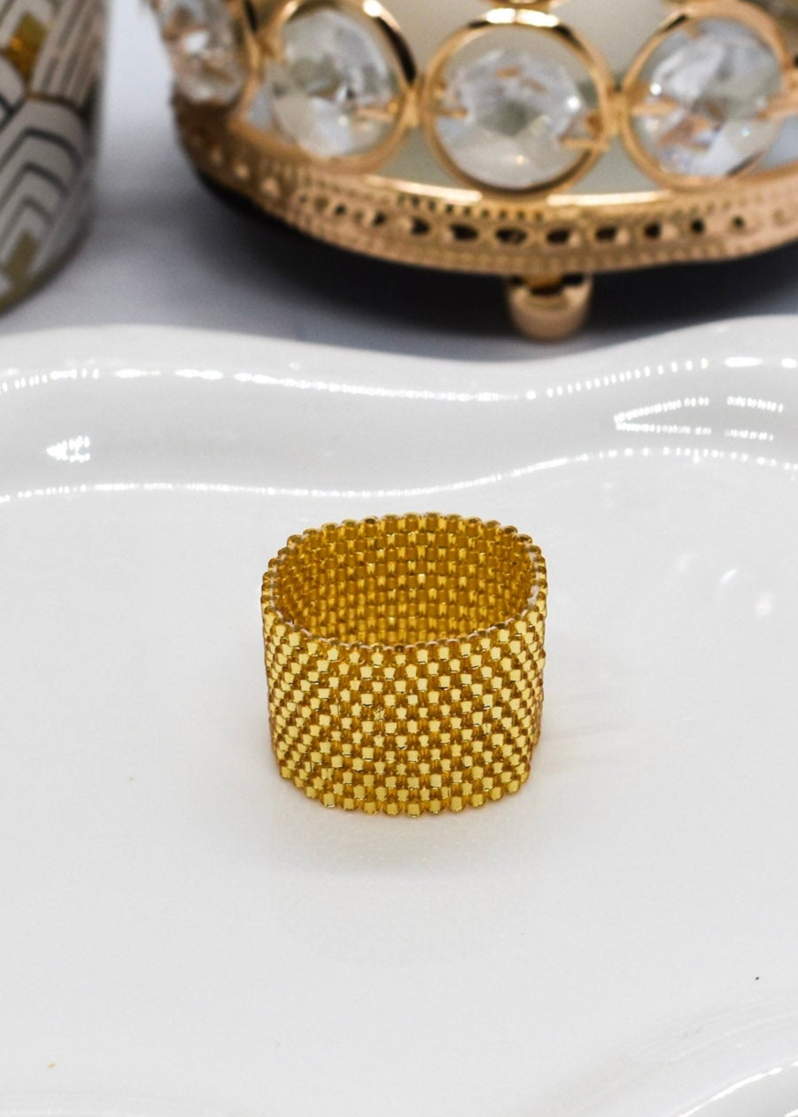 Gold beaded ring on a white surface with a decorative candle in the background