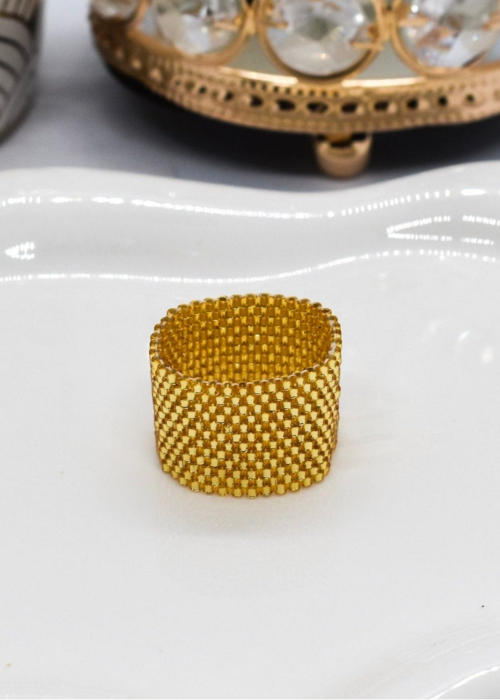 Gold beaded ring on a white surface with a decorative candle in the background