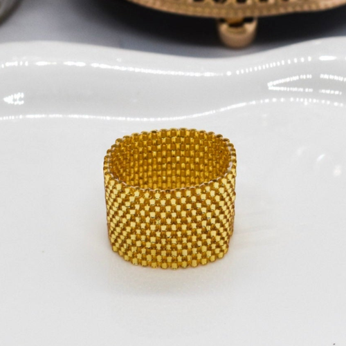 Gold beaded ring on a white surface with a decorative candle in the background